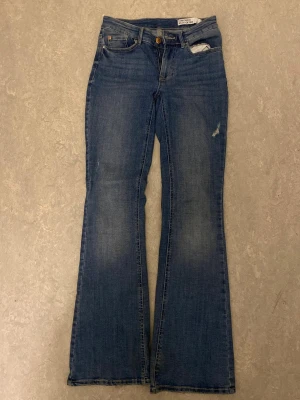 Blå bootcut jeans från Vero Moda i storlek s/32 - Mörkblåa jeans i storlek s/32.Snygga blå jeans från Vero Moda med klassisk bootcut-passform och fem fickor. Jeansen har en mörkblå tvätt med lätt slitning och dragkedja med knapp framtill. Materialet är jeans och de har en normal midja. Perfekta för dig som gillar retrovibbar och bekväm stil.