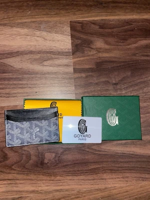 G-yard grå plånbok med mönster - Säljer en stilren grå plånbok från G-yard med ikoniskt grafiskt mönster i vitt. Plånboken har flera fack för kort och detaljer i svart skinn. Kommer med originalförpackning och certifikat. Perfekt för dig som gillar exklusiva accessoarer. Har 2 st och skriv gärna för mer bilder osv!