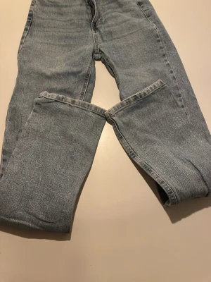 STR ljusblå jeans straight fit - Klassiska jeans i ljusblå tvätt med raka ben och hög midja. Jeansen har fem fickor, knappgylf och subtila slitningar på bakfickorna för en avslappnad vibe. Tillverkade i robust denim som ger en tidlös look.