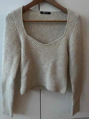 Beige stickad tröja Gina Tricot - Säljer en beige stickad tröja från Gina Tricot i storlek S. Tröjan har en djup, rundad halsringning och ribbad struktur med snygga detaljer framtill. Lite kort så passar snyggt till jeans med låg midja. Passar både vardagligt och vid andra tillfällen