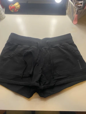 Svarta shorts från Björn Borg - Säljer ett par svarta shorts från Björn Borg med snörning i midjan och två fickor fram. De är tillverkade i mjuk bomull och har en normal passform. Perfekta för träning eller chill dagar. Diskret logga på ena fickan.