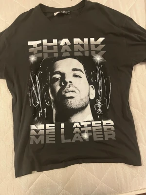 En DRAKE tröja - Grå t-shirt med tryck och metallictext - Cool drake svart t-shirt med stort tryck framtill och texten 'THANK ME LATER' i metallic-silver. Oversized passform och rund halsringning. Perfekt för dig som gillar statement-plagg och streetstyle. Perfekt för drake fans 