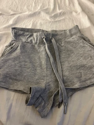 Grå mjuka shorts från H&M Divided - Säljer ett par grå shorts från H&M Divided i storlek XS. De har en loose passform, bred resår i midjan och snörning framtill. Materialet är mjukt med 76% bomull och 24% polyester, perfekt för chill dagar eller träning.