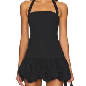 Svart kort klänning med halterneck - Snygg svart kort klänning med halterneck som knyts med rosett vid nacken och volang nedtill. Klänningen har en rak överdel och en lekfull, bubblig kjol som ger en cool och ungdomlig vibe. Perfekt för dig som gillar stilrena plagg med en twist. Hittar inte hemsidans originella annons men ser ut exakt som denna bild, skriv privat för egna bilder! Jätte fin! Endast använd 3 ggr