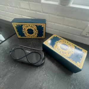 Mörkblå Versace Parfums necessär - Riktigt snygg oanvänd mörkblå neccesär från Versace Parfums med silverfärgad dragkedja och stilren design. Necessären har ett dekorativt mönster på framsidan och ett praktiskt handtag med Versace-detalj. Perfekt för att hålla ordning på dina produkter. Vid köp ingår box, en Versace parfym flaska! Vid intresse bara att höra av sig! 