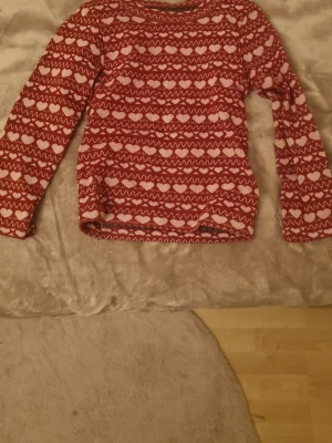 Röda leggings med vintermönster, stl S. och röd tröja med vintermönster, storlek 6år(jag bär xs och den är töjbar!) - Säljer ett par röda leggings med vita hjärtan, snöflingor och zigzag-mönster. Materialet är mjukt och stretchigt, 98% polyester och 2% elastan. Perfekt för mysiga vinterdagar och julstämning. Supersnygga och bekväma att ha på sig.