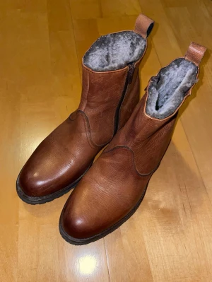 Bruna fodrade boots från Roberto Ley - Säljer ett par bruna boots från Roberto Ley med mjukt grått foder och grov sula. De är nog använda en gång ute men är i jättebra skick. De är tillverkade av äkta läder för hand i Spanien. Skorna har dragkedja på sidan och är tillverkade i skinn, perfekta för kalla dagar. Snygg rund tå och praktisk flik baktill för enkel påtagning. Priset är inte hugget i sten. Skriv vid minsta fundering! 