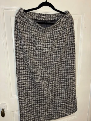 Rutig långkjol från Jyothi - Säljer en svartvit långkjol från Jyothi med klassiskt rutigt mönster. Kjolen har rak passform och är gjord i ett tjockare, strukturerat material som känns både stilrent och trendigt. Perfekt för dig som gillar tidlös design med en twist. Säljer även tillhörande topp & tröja med krage separat.