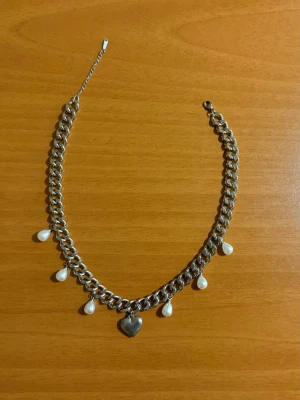 Silvrigt t halsband med hjärthänge och droppformade pärlor - Matchande örhängen finns i en separat annons  Finns även i guldpläterad variant.  Material: 18K guldplätering på rostfritt stål Bredd: 9 mm Längd: 38-43cm Nickelfria och handgjorda.