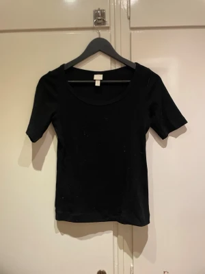 Svart enkel topp med kort ärm - En basic svart topp från H&M med rund halsringning och korta ärmar. Modellen är figurnära och passar perfekt till jeans eller kjol. Tillverkad i mjukt bomullsmaterial som känns skönt mot huden.