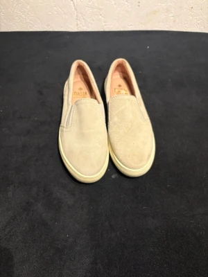Beige slip-on sneakers från Dasia - Snygga slip-on sneakers från Dasia i beige mocka med elastiska paneler på sidorna för enkel påtagning. Skorna har en vit, platt sula och rund tå. Perfekta för dig som gillar stilrena och bekväma skor till vardags.