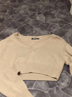 Beige croppad stickad tröja Gina Tricot - Säljer en beige croppad stickad tröja från Gina Tricot med v-ringad hals och långa ärmar. Tröjan har bred ribbad kant vid midjan och är perfekt för lager-på-lager. Enkel och snygg design som passar till jeans eller kjol.