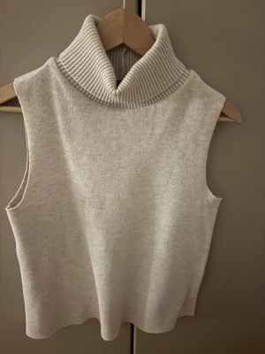 Beige polotopp från Zara - Säljer en jättetrendig beige polotopp från Zara i storlek M. Toppen är ärmlös med en bred, ribbad polokrage och har en mjuk stickad känsla. Säljs inte längre! Inte alls stickig!! Skriv privat för mer information!!