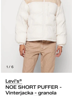 Levi's beige/vit pufferjacka - Säljer en kort pufferjacka från Levi's i snygg beige och vit färg. Jackan har hög krage, dragkedja framtill och två fickor. Oversized passform och quiltad design gör den både trendig och varm. Perfekt för kalla dagar när du vill ha en chill look.