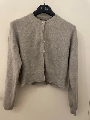 Grå kofta från Gina Tricot - En stilren grå kofta från Gina Tricot. Koftan har rund halsringning, långa ärmar och knäppning med små vita knappar framtill. Perfekt till lager på lager och enkel att matcha med olika outfits.