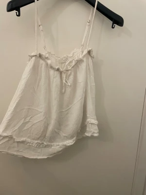 Vit linnetopp från Sisters Point - Supersöt vit linnetopp från Sisters Point med tunna justerbara axelband och volangdetaljer längs kanterna. Toppen har en liten knytning framtill och sopiga rynkade detaljer upptill och nedtill. Perfekt för varma dagar och en chill look.priset går att diskutera. 