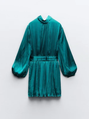 Turkos kort klänning med ballongärm - Snygg turkos kort klänning med glansigt tyg och ballongärmar. Klänningen har en markerad midja och ett elegant fall. Perfekt för dig som gillar att sticka ut med färg och stil. Materialet känns lyxigt och har en lätt skimrande yta.