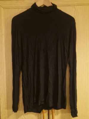 Svart polotopp från Lager157, storlek M - Svart långärmad polotopp från Lager 157, med klassisk hög krage och enkel design. Tunn och mjuk kvalitet som känns skön mot huden, perfekt att styla lager på lager. Passformen är normal och toppen är enfärgad utan detaljer. Kolla gärna in mina andra annonser för samfrakt 😊