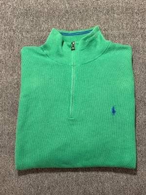 Grön stickad half zip från Polo Ralph Lauren - Snygg grön stickad tröja från Polo Ralph Lauren i storlek XXL. Tröjan har half zip framtill, långärmad design och klassisk blå logga broderad på bröstet. Perfekt för dig som gillar en loose passform och vill ha något stilrent med lite sportig vibe.
