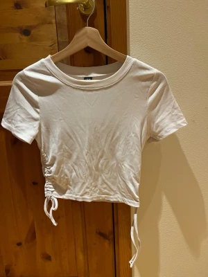 Vit magtröja - Vit enkelt ribbad magtröja med band på båda sidor om midjan som man själv kan anpassa hur kort tröjan är. Skön i materialet och sparsamt använd. Djur och rökfritt hem.
