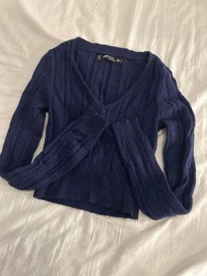 Marinblå stickad kofta från FB Sister - Snygg marinblå stickad kofta från FB Sister i storlek XS. Tröjan har v-ringad hals, ribbade muddar och ett kabelstickat mönster som ger en cool look. Perfekt att slänga på sig när det är lite kyligt ute.