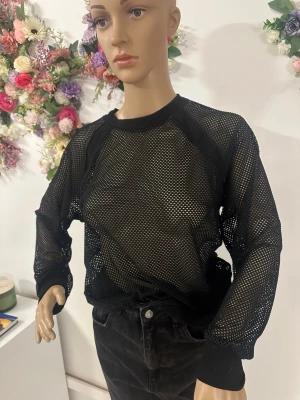Svart mesh långärmad topp - Säljer en svart långärmad mesh topp med rund halsringning. Toppen är helt genomskinlig med stora nätmaskor och har svarta kantband vid hals och ärmslut. Perfekt att styla lager på lager för en edgy look.