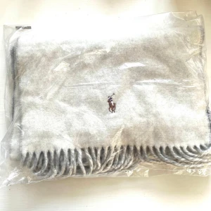 Ny Polo Ralph Lauren grå och vit halsduk, storlek ONE SIZE - Vändbar ljusgrå och vit halsduk med fransar som är tillverkad i Italien. Den har en broderad logotyp av en polospelare.Dubbelsidig halsduken gör också att det ser ennu snyggare tillsammans. Perfekt present, julklapp eller gåva :) passar män och kvinnor.  Ordpris:1595kr(Se sista bilden).  Bilderna togs personligen av mig, vilket säkerställer att du ser exakt den produkt du köper.Vänligen observera att jag inte har öppetköp.Skickar endast med PostNord.
