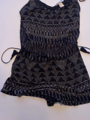 Svart och vit mönstrad byxdress - Säljer en svart byxdress med vitt geometriskt mönster och knytband i midjan. Lätt och luftig modell, perfekt för varma dagar. Materialet känns mjukt och bekvämt mot huden. Passar dig som gillar en avslappnad men ändå snygg stil.