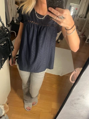 Mörkblå blus - Säljer en mörkblå blus från SHEIN i storlek M. Blusen har korta ärmar, broderade hålmönster och en fin spetsdetalj upptill. Den är tillverkad i mjuk polyester och har en luftig, loose passform som ger en avslappnad vibe.