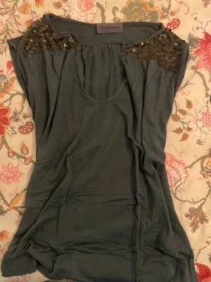 Grå topp med paljetter Zadig & Voltaire - Snygg grå topp från Zadig & Voltaire med paljettdetaljer på axlarna. Modellen är ärmlös och har en rundad halsringning. Toppens material känns mjukt och lätt, perfekt för att lyfta din outfit med lite extra glans.