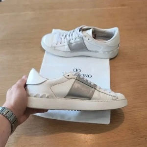 Valentino Garavani vita sneakers - 39 - Valentino sneakers i vitt med silverdetaljer i storlek 39. Ikonisk modell med exklusiv känsla som passar perfekt till både vardag och mer uppklädda outfits. Använda och i använt skick med normalt slitage, vilket framgår av bilderna. Äkta. Se bilder för skick och detaljer. Tveka inte att höra av dig vid frågor.