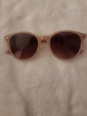 Solglasögon  - Säljer ett par beige rosa solglasögon ögon. Nästan aldrig använda och är i ett väldigt bra skick. Den har inga detaljer på sidorna.