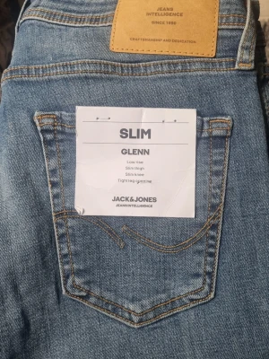 Jack & Jones Glenn Slim Fit Jeans W30 L32 - Slim fit jeans från Jack & Jones i modellen Glenn. Ljusblå tvätt, låg midja och smal passform hela vägen ner till benslutet. Klassisk femficksdesign och snygga kontrastsömmar. Perfekta för dig som gillar en tajtare look.