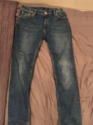 Blå jeans från Gant med raka ben - Säljer ett par klassiska blå jeans från Gant med snygga slitningar och kontrastsömmar. Modellen har raka ben och fem fickor, med Gant-logga på myntfickan och läderpatch bak i midjan. Perfekta till vardags och passar till det mesta.