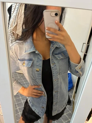 Ljusblå jeansjacka med fickor - Säljer en klassisk ljusblå jeansjacka med snygga detaljer som bröstfickor med knappar och markerade sömmar. Jackan har lång ärm och knäppning framtill. Perfekt att slänga över en t-shirt eller hoodie för en chill look.