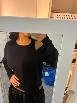 Svart offshoulder ribbad topp - Säljer en svart ribbad topp med lång ärm och offshoulder-detalj på ena sidan. Toppen har en croppad passform och är tillverkad i ett mjukt, stretchigt material som sitter snyggt på kroppen. 