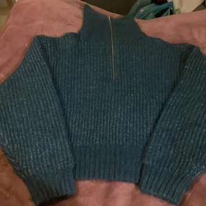 Blå stickad half zip från Gina Tricot - Mysig blå stickad tröja från Gina Tricot med hög krage och half zip-dragkedja. Tröjan har ribbad struktur och långa ärmar, perfekt för kyliga dagar. Snygg oversized look och passar till allt från jeans till kjol.