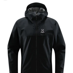 Svart vindjacka från Haglöfs dam L - Snygg svart vindjacka från Haglöfs i dammodell, storlek L. Jackan har hel dragkedja, huva och meshfoder på insidan för extra komfort. Perfekt för blåsiga dagar och outdoor vibes. Klassisk logga på bröstet och stilren design.