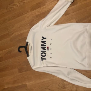 Vit sweatshirt från Tommy Jeans - Snygg vit sweatshirt från Tommy Jeans med stor logga framtill. Klassisk rund halsringning och långa ärmar. Perfekt för dig som gillar stilren och sportig look. Mjuk och skön, passar till jeans eller joggers.