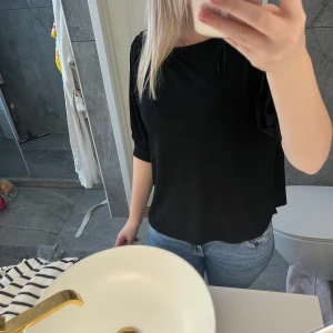 Svart blus med trekvartsärm - En stilren svart blus med rund halsringning och trekvartsärmar. Modellen är rak och har en avslappnad passform, perfekt att matcha med jeans eller kjol. Enkel och tidlös design som funkar till många olika looks.