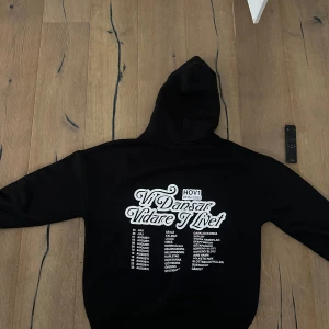 Svart Hov1 hoodie Vi Dansar Vidare - Svart hoodie från Hov1 med vit text 'Vi Dansar Vidare I Livet' och turnédatum på ryggen. Framtill finns en liten broderad krona på bröstet . Den är endast använd 1 gång, högsta bud ligger på 1900 så buda från de