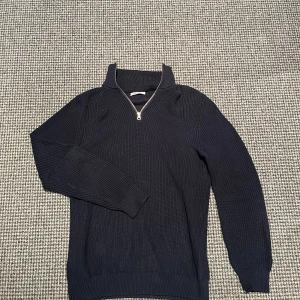Mörkblå stickad half zip-tröja från Zara - Säljer en mörkblå stickad tröja från Zara med half zip-dragkedja och hög krage. Tröjan är ribbstickad och har långa ärmar, perfekt för kyligare dagar. Enkel och stilren design som funkar till många outfits. Hör av dig vid minsta fundering!