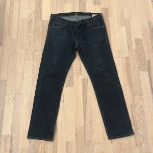 Mörkblå jeans från Lee - Snygga mörkblå jeans från Lee med klassisk femficksdesign och raka ben. Jeansen har kontrastsömmar och Lee-logga på bakfickan. Perfekta för dig som gillar en tidlös och clean look. Materialet är slitstarkt denim i bomull.