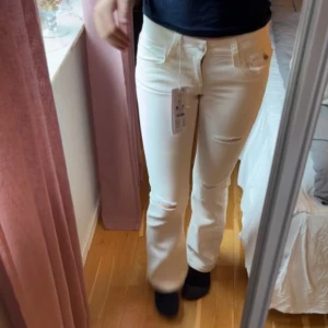 Vita bootcut jeans med slitningar - Säljer ett par vita jeans med bootcut-snitt och snygga slitningar vid knäna. Byxorna har klassiska fickor både fram och bak samt hällor för bälte. Perfekta för dig som vill ha en fräsch och trendig look.