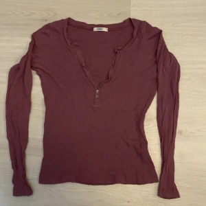 Ljuslila långärmad topp med knappar - Superskön ljuslila långärmad topp från C&C med v-ringning och tre knappar framtill. Tunt och mjukt bomullsmaterial som sitter tajt men ändå bekvämt. Perfekt till jeans eller kjol för en chill look. Storlek S men är väldigt stretchig