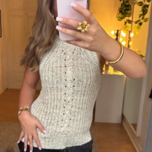 Stickad ärmlös topp - Supersnygg stickad topp från Object i beige ton, med ribbad struktur . Modellen är ärmlös med hög hals och sitter figurnära runt kroppen. Jätte fint skick. De första bilderna är tagna i naturligtljus och visar färgen. Läs bion innan köp.  Inga defekter