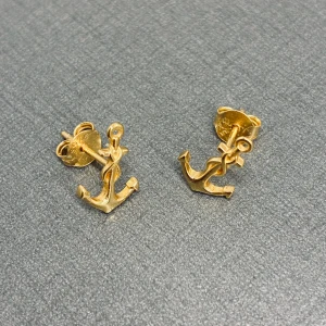 Guldiga örhängen med ankare - Snygga små örhängen i form av ankare, tillverkade i guldfärgat material. Perfekta för dig som gillar marina detaljer och vill ha något unikt och stilrent i öronen. Passar både till vardagslooken och när du vill sticka ut lite extra.