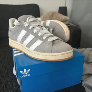 Adidas Campus grå  - Snygga Adidas Campus sneakers i ljusgrå mocka med klassiska vita ränder på sidorna och vit sula med gummidetalj. Skorna har rund tå, snörning och en stilren retrovibe. Knappt använda, inga defekter