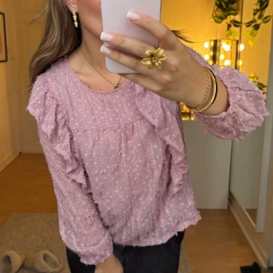 Rosa blus - Jätte fin blus med mycket detaljer. Blusen har volanger och små vita prickar, den har också två lager tyg förutom på armarna som gör att de ser mer genomskinliga ut vilket gör den ännu finare. Den är i jätte fint skick och har inga defekter, är knappt använd. Den är köpt på kappahl i storlek 164 men sitter som en xs/s tröja. Läs i bion innan köp.