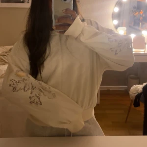 Vit hoodie med blommigt mönster - Säljer denna super fina collegetröja med mönster vid ärmarna 